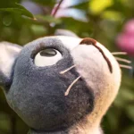 A vintage felt plushie cat in a garden looks with curiosity at something above, macro photogr...webp
